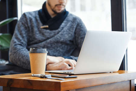 Young attractive man with laptop and modern electronic watches drinking coffee in modern bright cafe at business lunch. Freelancer or business man working on laptop.の写真素材