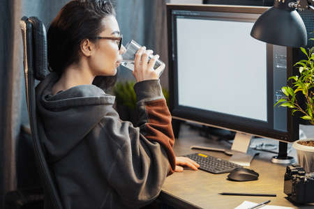 Young attractive woman freelancer designer working on pc at home. Concept of freedom and creativity. Home office. Computer with blank screen monitor. Casual dress.の写真素材