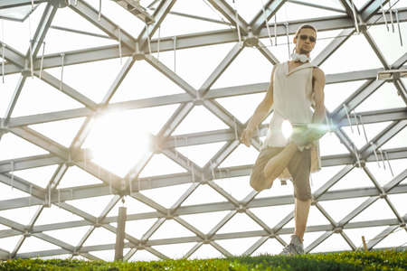 Attractive athletic man practicing yoga outdoors in modern park.