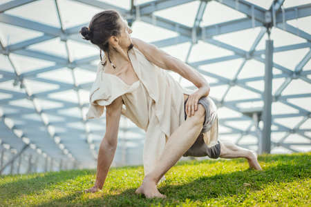 Close up of attractive athletic man practicing yoga and warming up in modern park at green grass outdoors.の写真素材