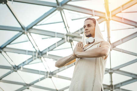 Close up of attractive athletic man practicing yoga and warming up outdoors in modern park under the glass dome.の写真素材