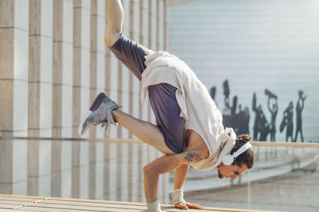 Attractive athletic man practicing yoga with maces outdoors in park next to modern building.の写真素材