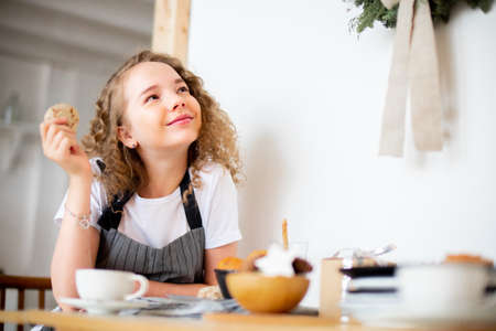Young cute curly girl eating homemade oat cookie and smiling. Family love and care concept.の写真素材