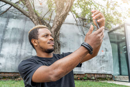 Close up of dark-skinned man in black T-shirt making selfie on mobile phone.の写真素材