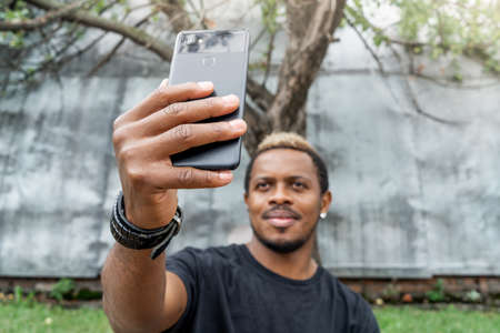 Close up of dark-skinned man in black T-shirt making selfie on mobile phone.の写真素材