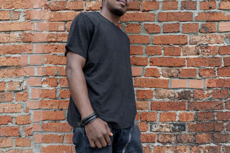 Young attractive dark-skinned man in black T-shirt on red bricked background.の写真素材