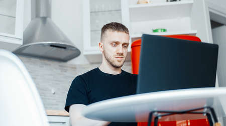 Handsome pensive man working on laptop in modern bright apartments.
