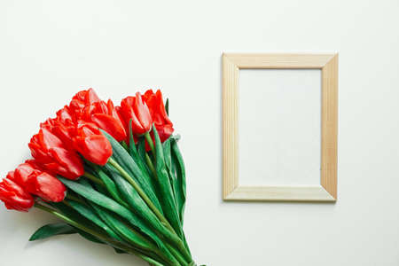 Flatlay of tulips and blank white photo frame on white background. Summer or spring time. International women day. Copy space. Empty space.の写真素材