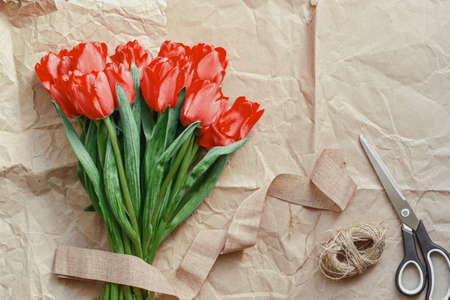Flatlay of tullips and craft wrapping paper, ribbon, scissors and present. Summer or spring time. International women day. Copy space. Empty space.の写真素材