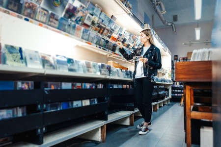 Young attractive woman choosing vinyl record in music record shop. Melomaniac or music addict concept.の写真素材