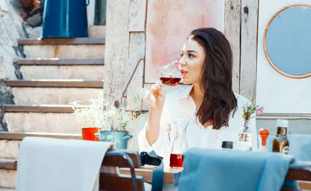 Young beautiful woman drinking red wine at street cafe in European town. Wine degustation. Traveler and blogger.の写真素材