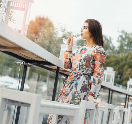 Young beautiful brunette woman in Evening Dress drinking sparkling champagne at the beach in street cafe.の写真素材
