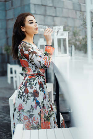 Young beautiful brunette woman in Evening Dress drinking sparkling champagne at the beach in street cafe.の写真素材