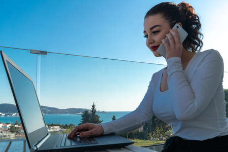 attractive woman working on laptop on balcony and enjoying beautiful landscape panorama. View on Sea, mountains and town. Freelancer work place. Connection and availability in every part of planetの写真素材