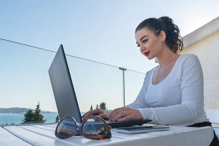 attractive woman working on laptop on balcony and enjoying beautiful landscape panorama. View on...