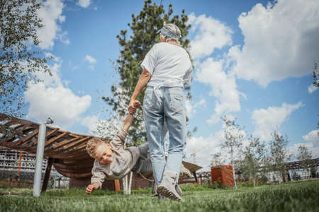Young mum turning around, whirling and having fun with her sons at green modern park. Happy family concept.の写真素材