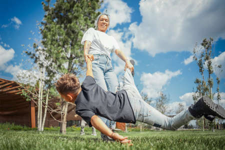 Young mum turning around, whirling and having fun with her sons at green modern park. Happy family concept.の写真素材