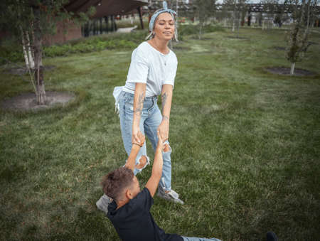 Young pretty mum turning around, whirling with her son at park. Happy family concept. Family is on foreground and focus, park is blurred.の写真素材