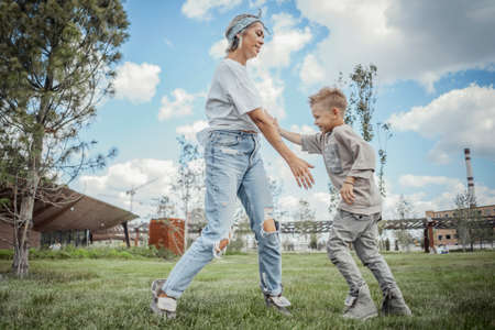 Young pretty mum turning around, whirling with her son at park. Happy family concept. Family is on foreground and focus, park is blurred.の写真素材