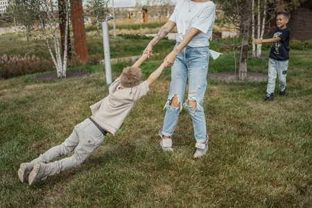 Young mum turning around, whirling and having fun with her sons at green modern park. Happy family concept.の写真素材
