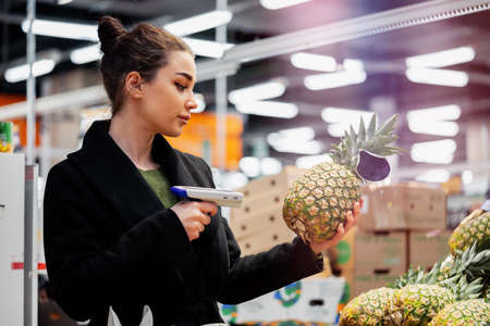 Young attractive woman holding bar code scanner and scanning products in store. Concept of modern...