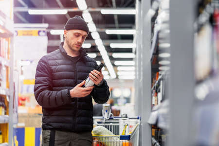 Young handsome man choosing wine in supermarket. Matter of wine choice.の写真素材