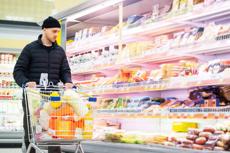 Young handsome man choosing products in supermarket. Matter of choice. Consumerism.の写真素材