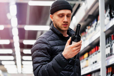 Young handsome man choosing wine in supermarket. Matter of wine choice.の写真素材