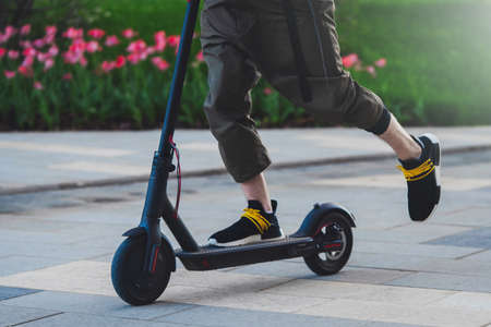 Close up of man riding black electric kick scooter at beautiful park landscape. Man is on...