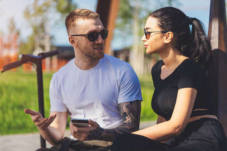 Couple of young man and woman sitting in park on wooden bench.の写真素材