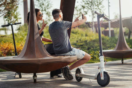 Couple of young man and woman sitting in park and making selfie.の写真素材