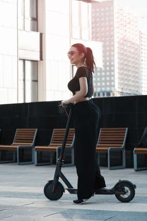 Young attractive woman riding electrick kick scooter at modern cityscape.の写真素材