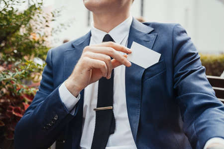 Close up of businessman putting blank business card in his blue jacket pocket. Side view.の写真素材