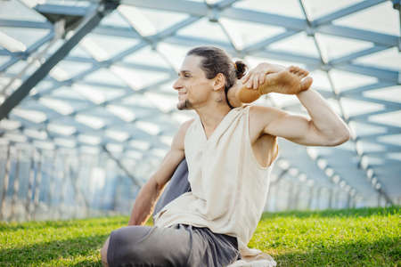 Close up of attractive athletic man practicing yoga and warming up outdoors.の写真素材