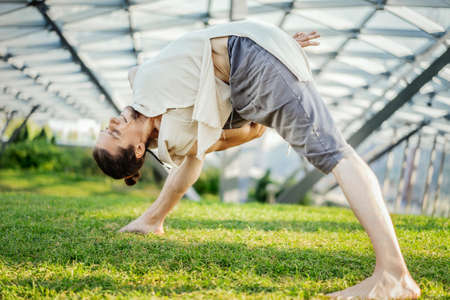 Close up of attractive athletic man practicing yoga and warming up outdoors.の写真素材