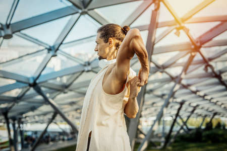 Close up of attractive athletic man practicing yoga and warming up outdoors in modern park under the glass dome.の写真素材