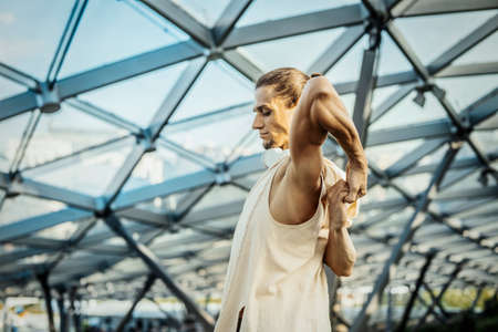 Close up of attractive athletic man practicing yoga and warming up outdoors in modern park under the glass dome.の写真素材
