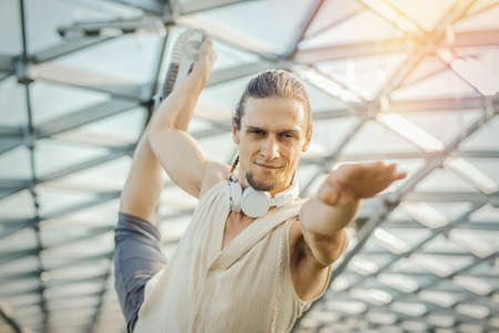 Close up of attractive athletic man practicing yoga and warming up outdoors in modern park under the glass dome.の写真素材
