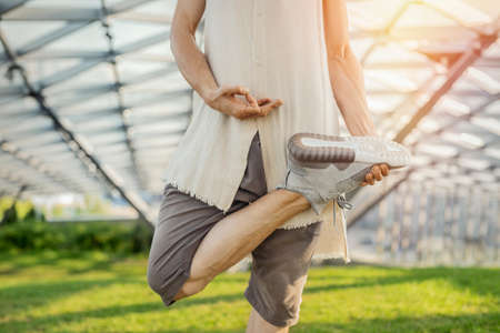 Close up of attractive athletic man practicing yoga and meditating in modern park at green grass outdoors.の写真素材