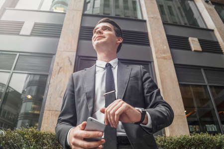 Close up of businessman next to skyscraper at downtown waiting for a meeting. Bottom view.の写真素材