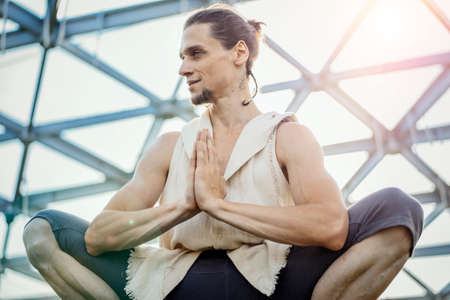 Close up of attractive athletic man practicing yoga and warming up outdoors in modern park under the glass dome.の写真素材