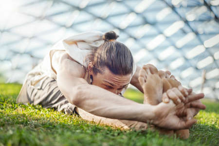 Close up of attractive athletic man practicing yoga and warming up outdoors.の写真素材