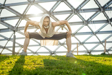 Attractive athletic man practicing yoga and warming up outdoors in modern park.の写真素材