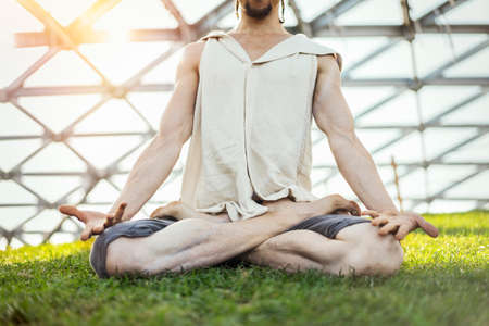 Close up of attractive athletic man practicing yoga and meditating in modern park at green grass outdoors.の写真素材