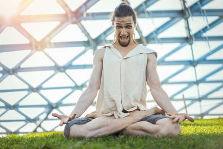 Close up of attractive athletic man practicing yoga and meditating in modern park at green grass outdoors.の写真素材