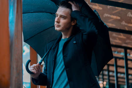 Young pensive handsome man with umbrella on rainy day going for a walk in park.の写真素材