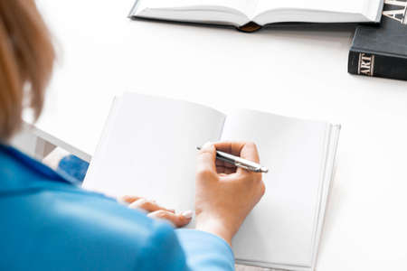 Young pensive attractive woman in formal attire makes some notes in notepad at library.