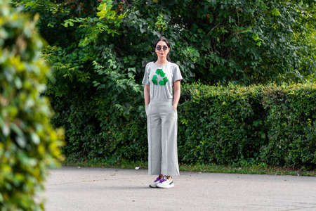 Young smiling attractive woman in gray t-shirt with recycle symbol in park.の写真素材