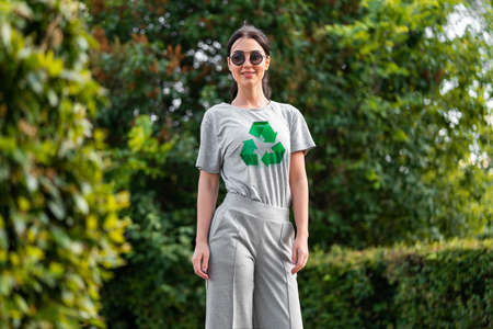 Young smiling attractive woman in gray t-shirt with recycle symbol in park.の写真素材