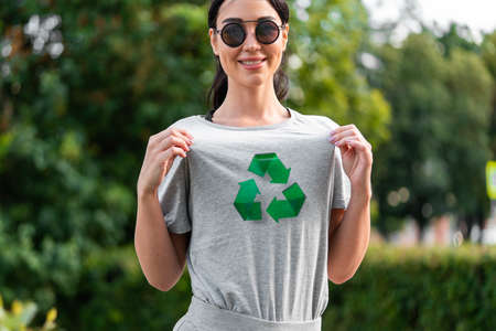 Young smiling attractive woman in gray t-shirt with recycle symbol in park.の写真素材